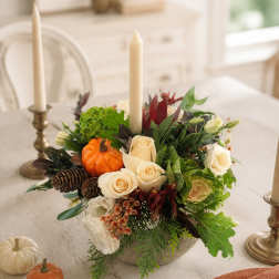 Autumn floral centerpiece with cream roses, candles, and small pumpkins in a low bowl