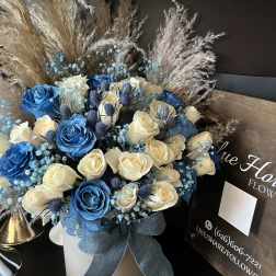 Blue and cream roses arranged in a white hatbox with a ribbon.