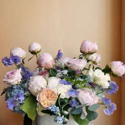 Pastel bouquet of roses, peonies, and blue flowers in a white vase