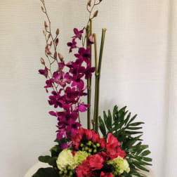 Tall floral arrangement with purple orchids and pink blooms in a low container