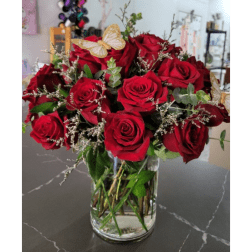 Red roses arranged in a clear glass vase with a butterfly accent