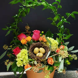 Floral arrangement with roses and hydrangea in a pot, topped with a bird nest and eggs