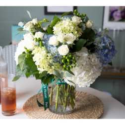 White and blue hydrangeas with white roses arranged in a clear glass cylinder vase