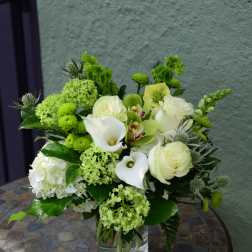 Arrangement of white roses, hydrangea, green orchids and calla lilies in a glass vase