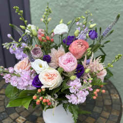 Pastel pink and white flower arrangement with purple accents in a white vase on a mosaic table.