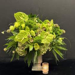 Lime green floral arrangement in a pedestal vase with a small candle
