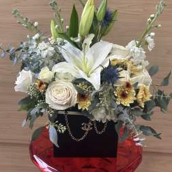White lilies and roses arranged in a red vase with greenery