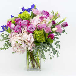 Tall pink and purple mixed flower arrangement in a clear rectangular glass vase