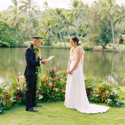 Bride and groom standing by tropical floral arrangements during a wedding ceremony