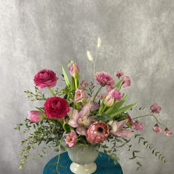 Pink and magenta flowers arranged in a white pedestal vase