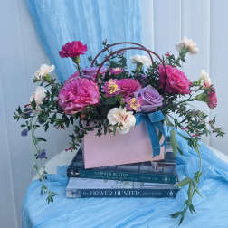 Pink and lavender roses with small white blooms in a pink box with a blue ribbon