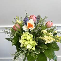 Spring bouquet with pink tulips, white daffodil, green hydrangea, and purple hyacinths in a white container