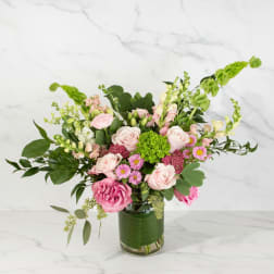 Arrangement of pink roses and mixed blooms with green hydrangea in a clear glass vase