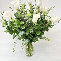 White roses arranged in a clear glass vase with greenery