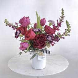 Pink and burgundy bouquet in a white vase with a striped ribbon