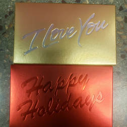 Two metallic gift boxes reading "I Love You" and "Happy Holidays"