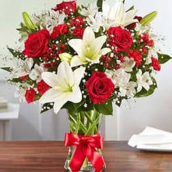 Bouquet of red roses and white lilies in a glass vase with a red ribbon