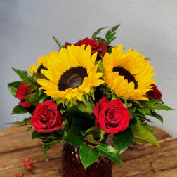 Arrangement of yellow sunflowers and red roses in a dark glass vase on a wooden table