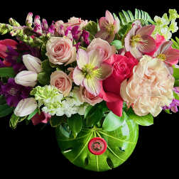 Mixed bouquet of pink roses, tulips, and hellebores in a green vase