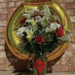 Bouquet of red and white flowers in a glass mug with a gold balloon behind it