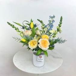 Mixed bouquet in a white vase with yellow, blue, and cream flowers