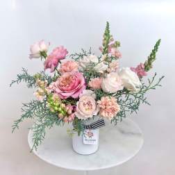 Pink and white roses arranged in a white vase with airy greenery