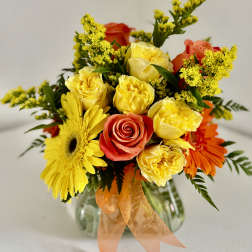 Mixed bouquet of yellow and orange flowers in a glass vase with an orange ribbon