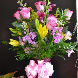 Pink roses and yellow lilies in a glass vase with a pink ribbon