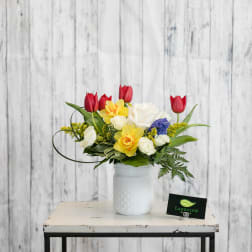 Mixed bouquet in a white ceramic vase with red tulips, yellow daffodils, and white roses