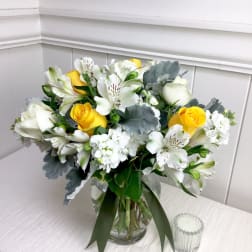 Yellow and white roses with white alstroemeria and soft gray foliage in a clear glass vase