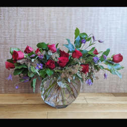 Red roses and purple bellflowers in a clear glass vase