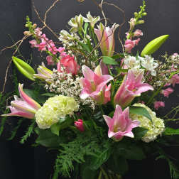 Pink lilies and mixed blooms arranged with curly branches in a vase
