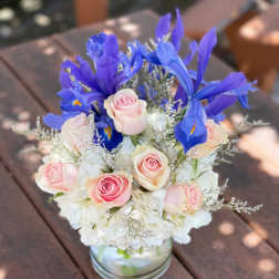Pink roses and blue irises arranged in a glass vase