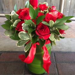 Red roses arranged in a green vase with a red ribbon