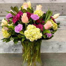 Mixed bouquet of roses, hydrangeas, and tulips in a clear glass vase