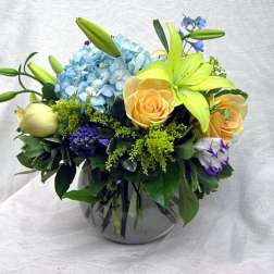 Mixed bouquet with blue hydrangea, yellow lilies, and peach roses in a glass vase