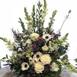 Tall floral arrangement with cream roses, white anemones, and pale snapdragons