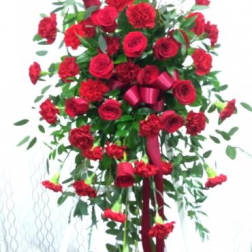 Tall standing spray of red roses and carnations with a burgundy ribbon