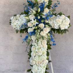White floral cross arrangement with blue accents on an easel