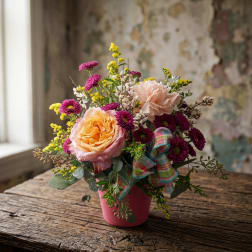 Pink and peach flowers arranged in a small pink pot with a plaid ribbon
