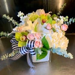 White and pink floral arrangement in a square vase with a striped ribbon