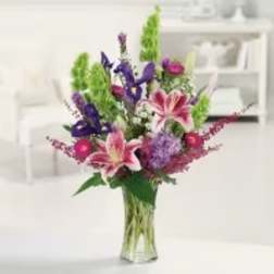 Mixed bouquet of pink lilies and purple flowers in a clear glass vase