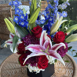 Bouquet of red roses, pink lilies, and blue delphinium in a black box