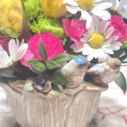 Colorful mix of yellow roses, pink carnations, and white daisies in a ceramic bird planter