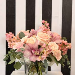 Pink roses and orchids arranged in a clear square vase.