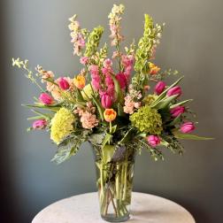 Tall mixed arrangement of pink and yellow tulips, green hydrangeas, and Bells of Ireland in a clear glass vase