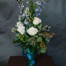 White roses and blue flowers arranged in a tall blue vase