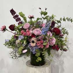 Large mixed bouquet in a dark green vase with pink, burgundy, and blue flowers