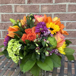Mixed bouquet in a clear glass vase with orange, yellow, purple, and green blooms