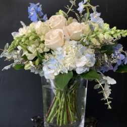 Bouquet of pale roses, hydrangeas, and blue flowers in a clear glass vase